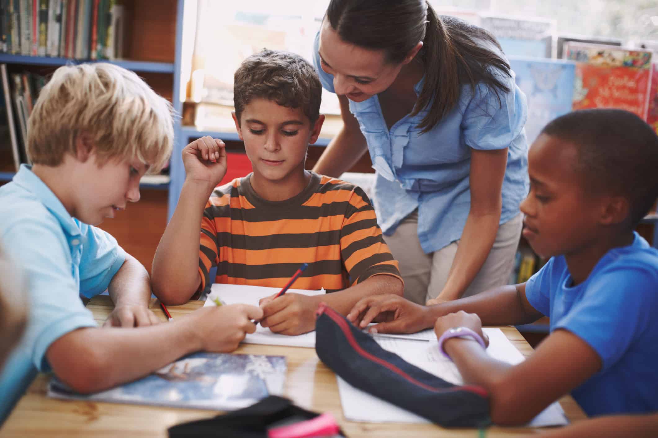 teacher in blue shirt smiles at boy with striped shirt and two other students