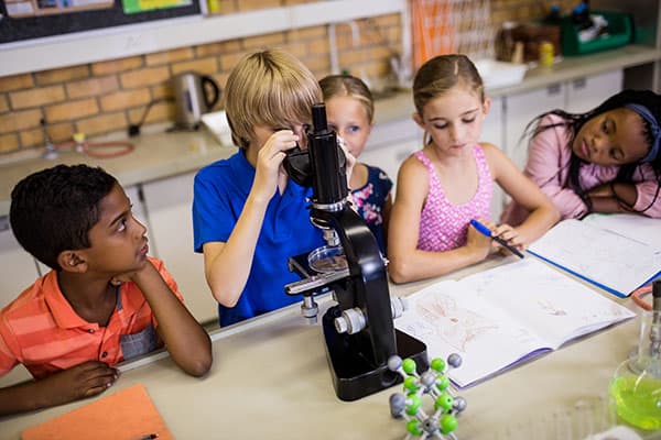 kids sitting in a classroom looking through a telescope